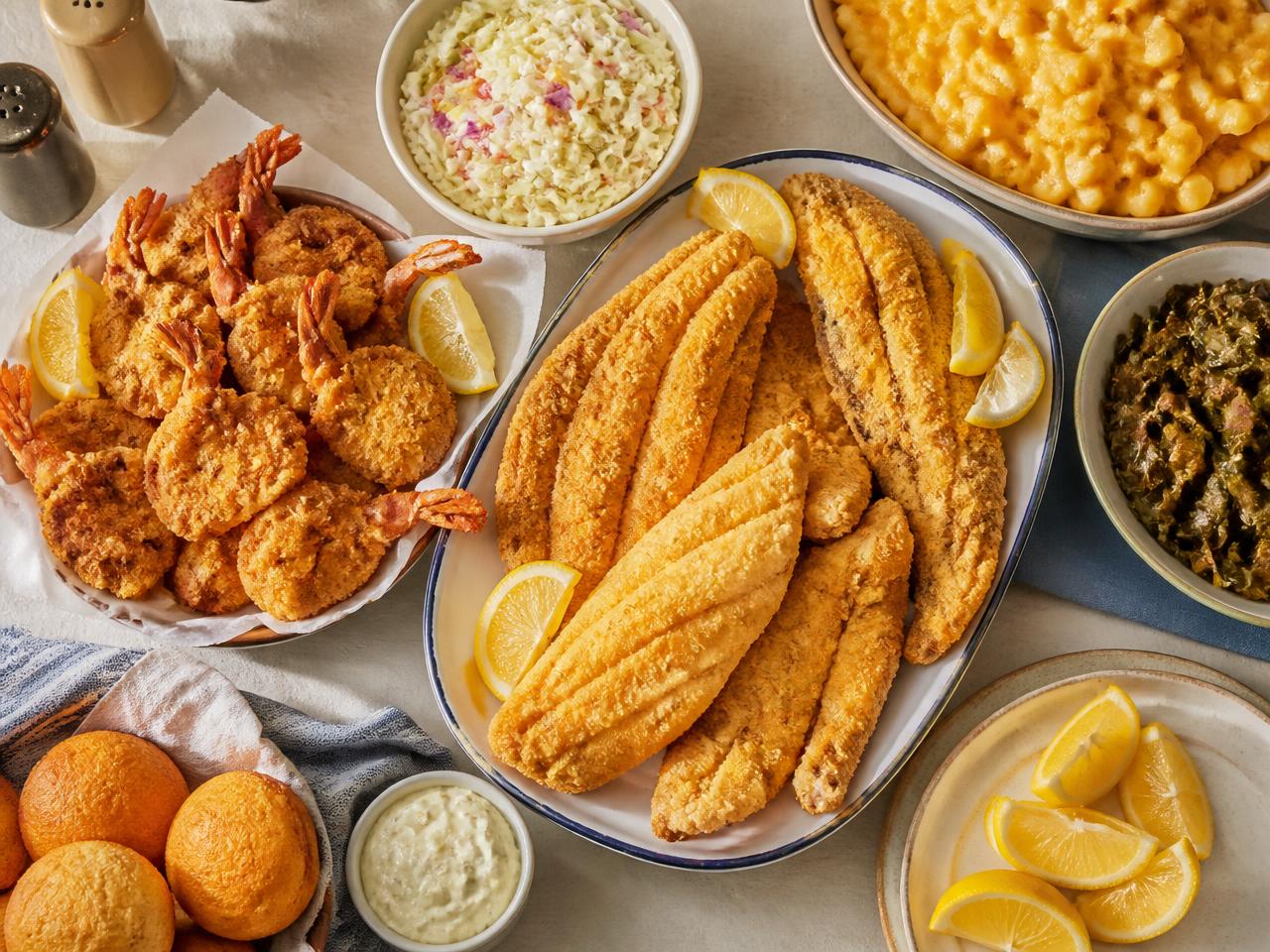 Overhead spread of fried fish fillets, battered shrimp, coleslaw, mac and cheese, collard greens and cornbread